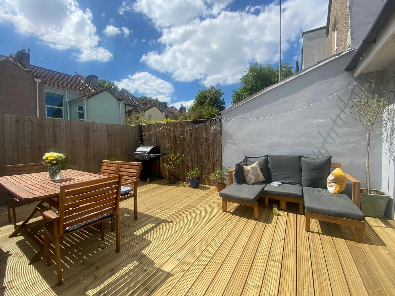 Completed timber decking in a sunlit garden, with lounge seating and festoon lights along the boundary fence