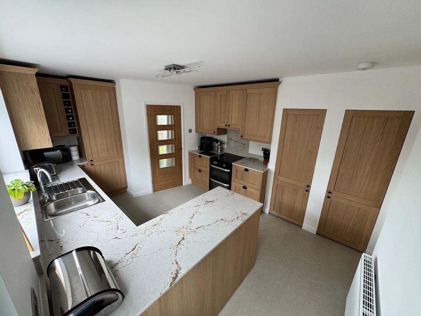 Recently completed light oak shaker kitchen with marble-effect worktops and integrated peninsula breakfast bar